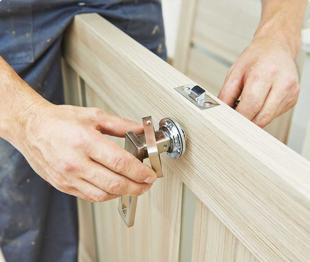 Handyman installing a modern door handle on a wooden door.