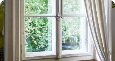 White-framed window with open curtains overlooking a lush green garden