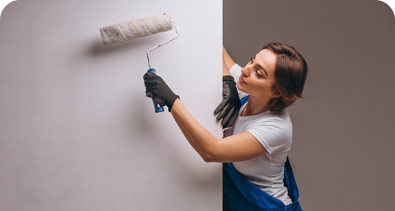 Female painter using a roller to paint a wall white while wearing gloves and overalls